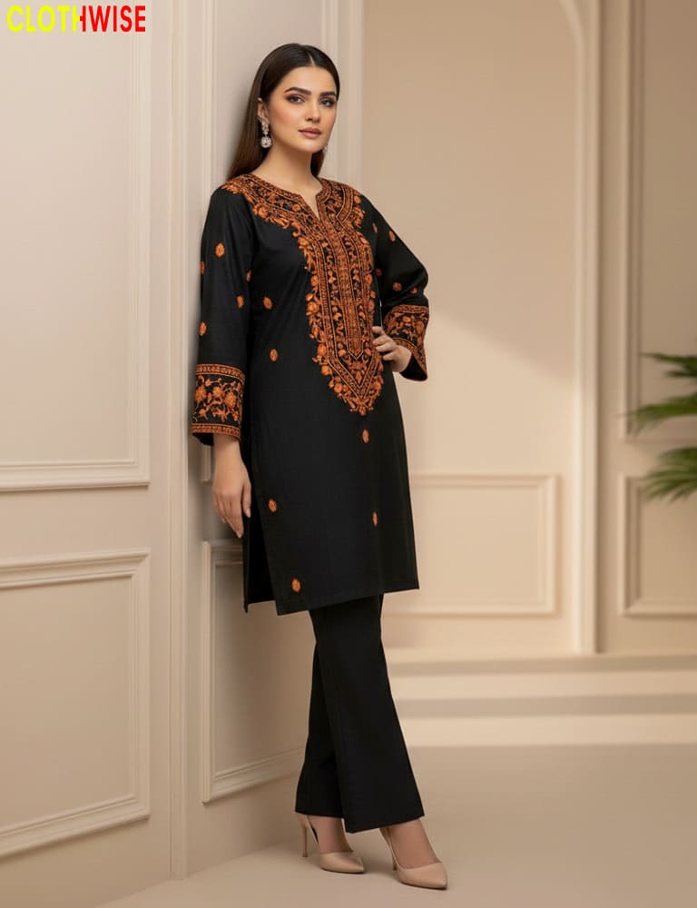 Woman wearing a black outfit with orange embroidery in an elegant interior setting.