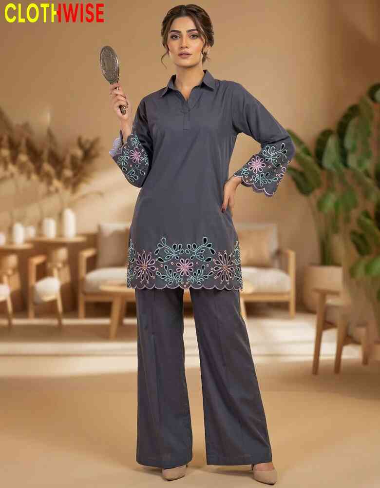 Woman in a gray outfit with floral embroidery holding a mirror indoors.