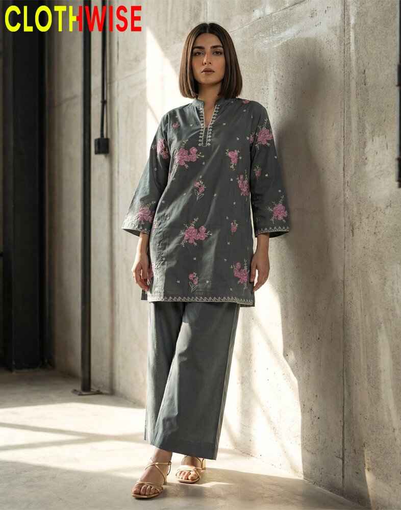 Woman wearing a gray floral patterned outfit against a concrete wall.