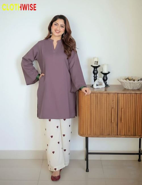 Woman wearing a purple top and white pants with heart patterns, standing in a room with a wooden cabinet.