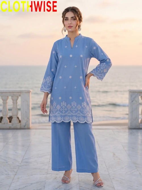 A woman modeling a light blue embroidered kurta and matching wide-leg pants set, standing on a marble walkway with the ocean and sunset in the background. The brand name 'CLOTHWISE' is displayed in the top left corner.
