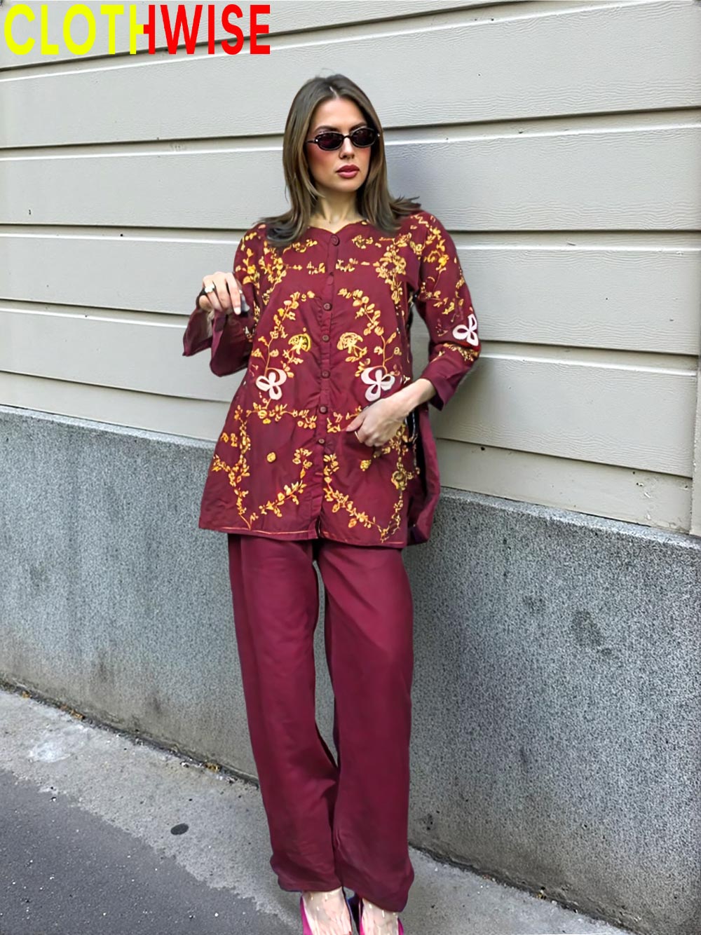 Woman wearing a maroon outfit with gold embroidery against a gray wall.