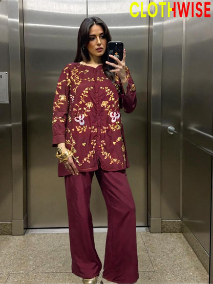 Woman taking a mirror selfie wearing a maroon outfit with gold patterns in an elevator.
