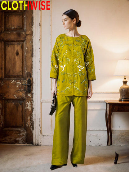 Woman wearing a green patterned outfit standing in a room with a wooden door and lamp.