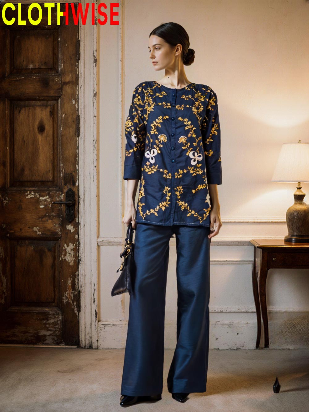 Woman wearing a navy blue outfit with gold embroidery in a room with wooden door and lamp.