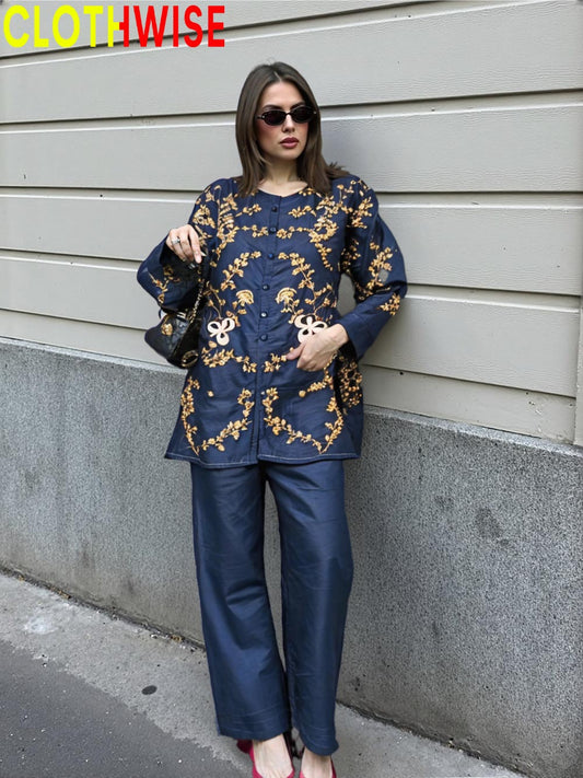 Woman in a blue embroidered outfit standing against a gray wall, with 'CLOTHWISE' branding.