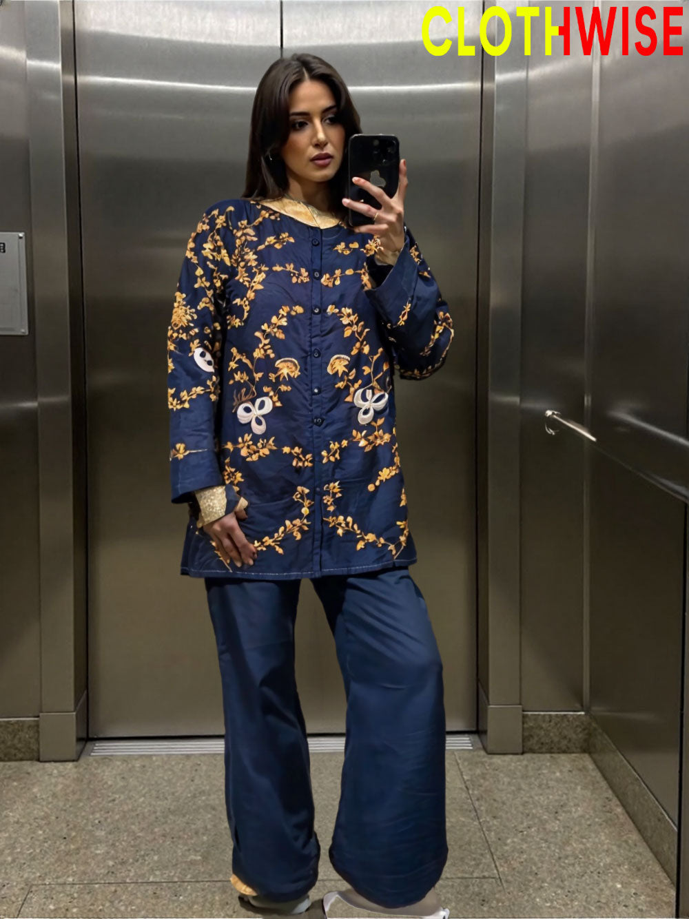 Woman taking a mirror selfie wearing a blue floral dress in an elevator.