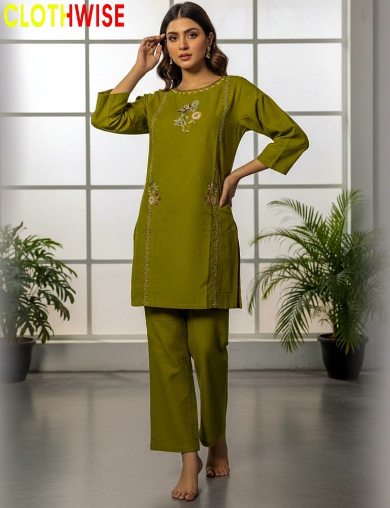 Woman wearing a green outfit with floral embroidery in a room with plants and a grid-patterned wall.