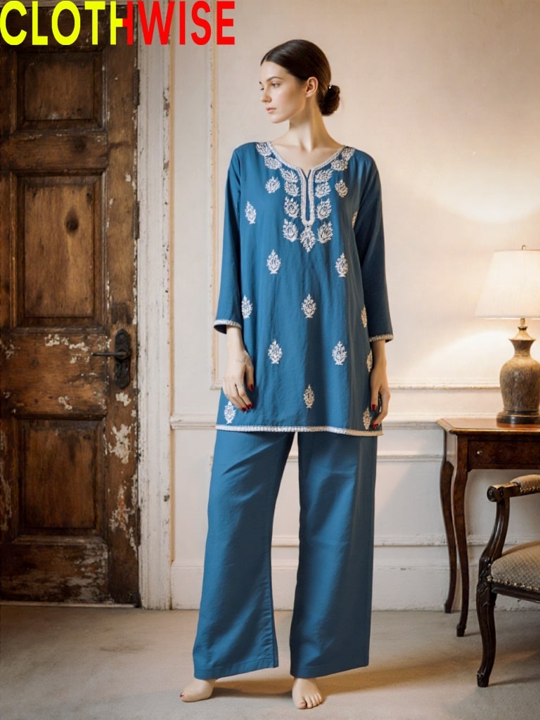 Woman wearing a blue embroidered outfit in a room with wooden door and lamp.