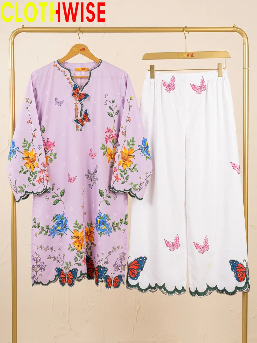 A two-piece women's outfit set from the brand CLOTHWISE, featuring a light purple tunic top with colorful floral and butterfly prints, and matching white wide-leg pants with pink butterfly prints and scalloped edges.