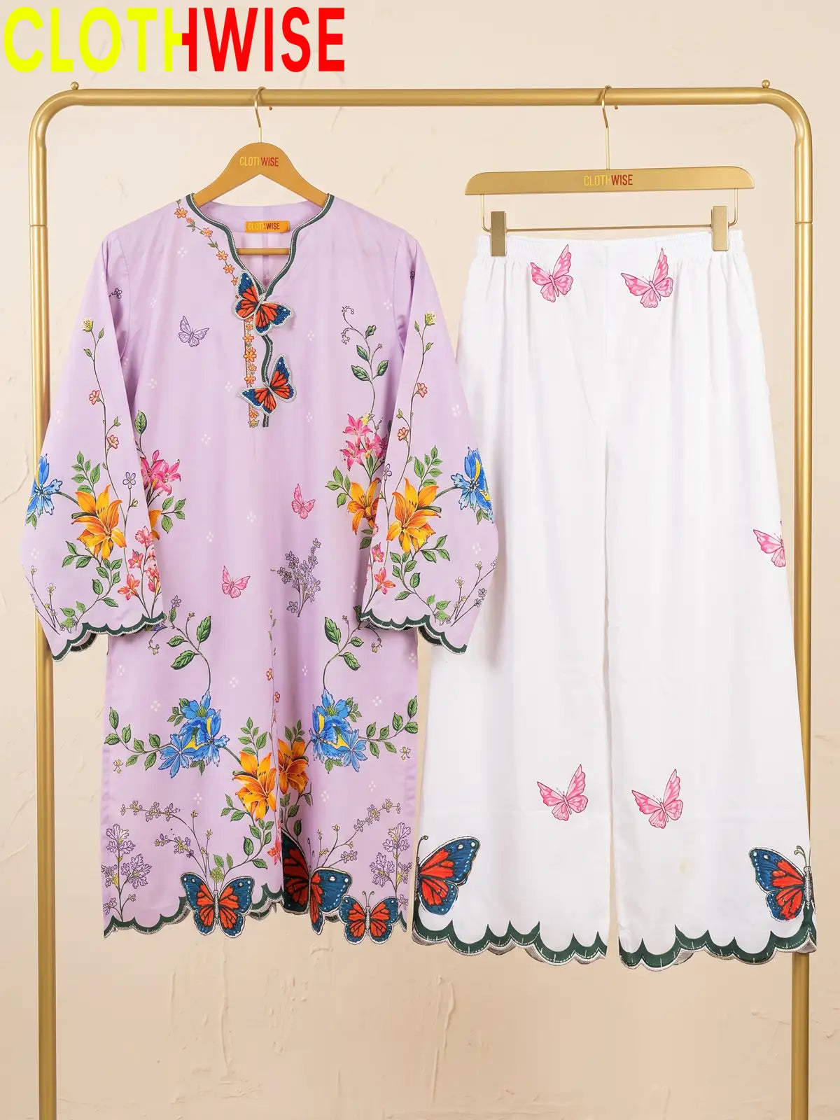 A two-piece women's outfit set from the brand CLOTHWISE, featuring a light purple tunic top with colorful floral and butterfly prints, and matching white wide-leg pants with pink butterfly prints and scalloped edges.