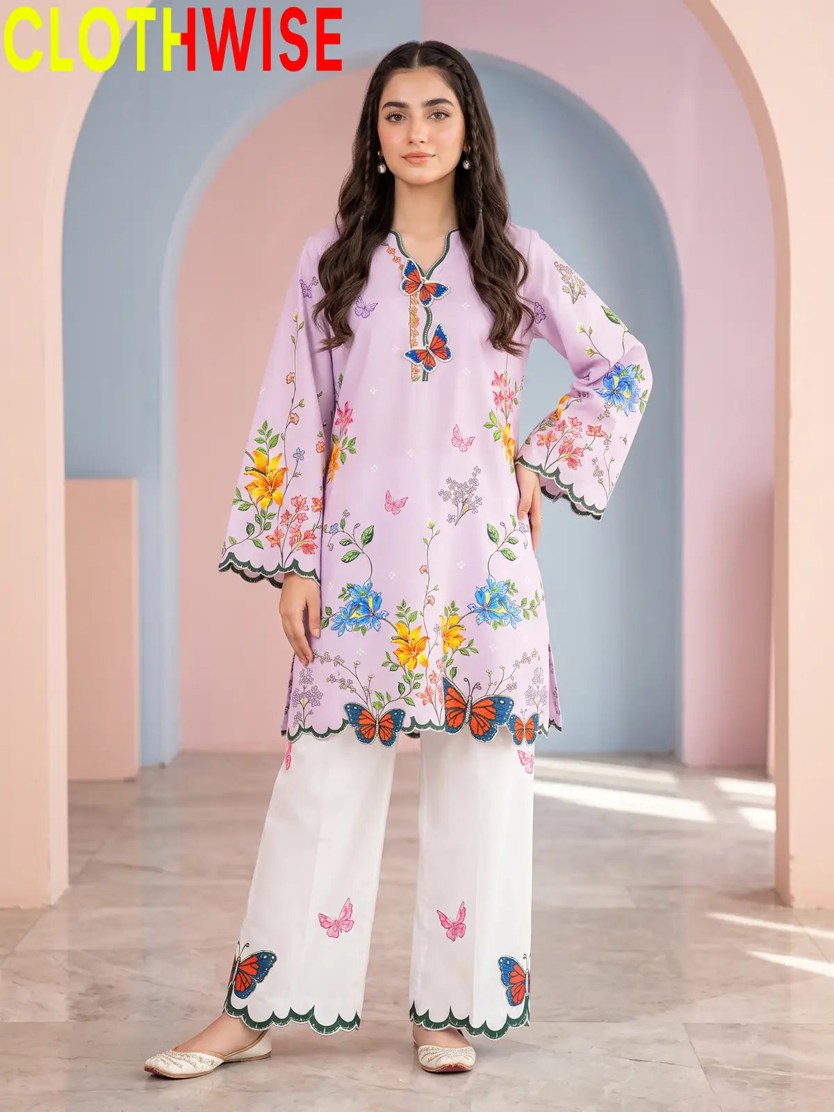 A two-piece women's outfit set from the brand CLOTHWISE, featuring a light purple tunic top with colorful floral and butterfly prints, and matching white wide-leg pants with pink butterfly prints and scalloped edges.