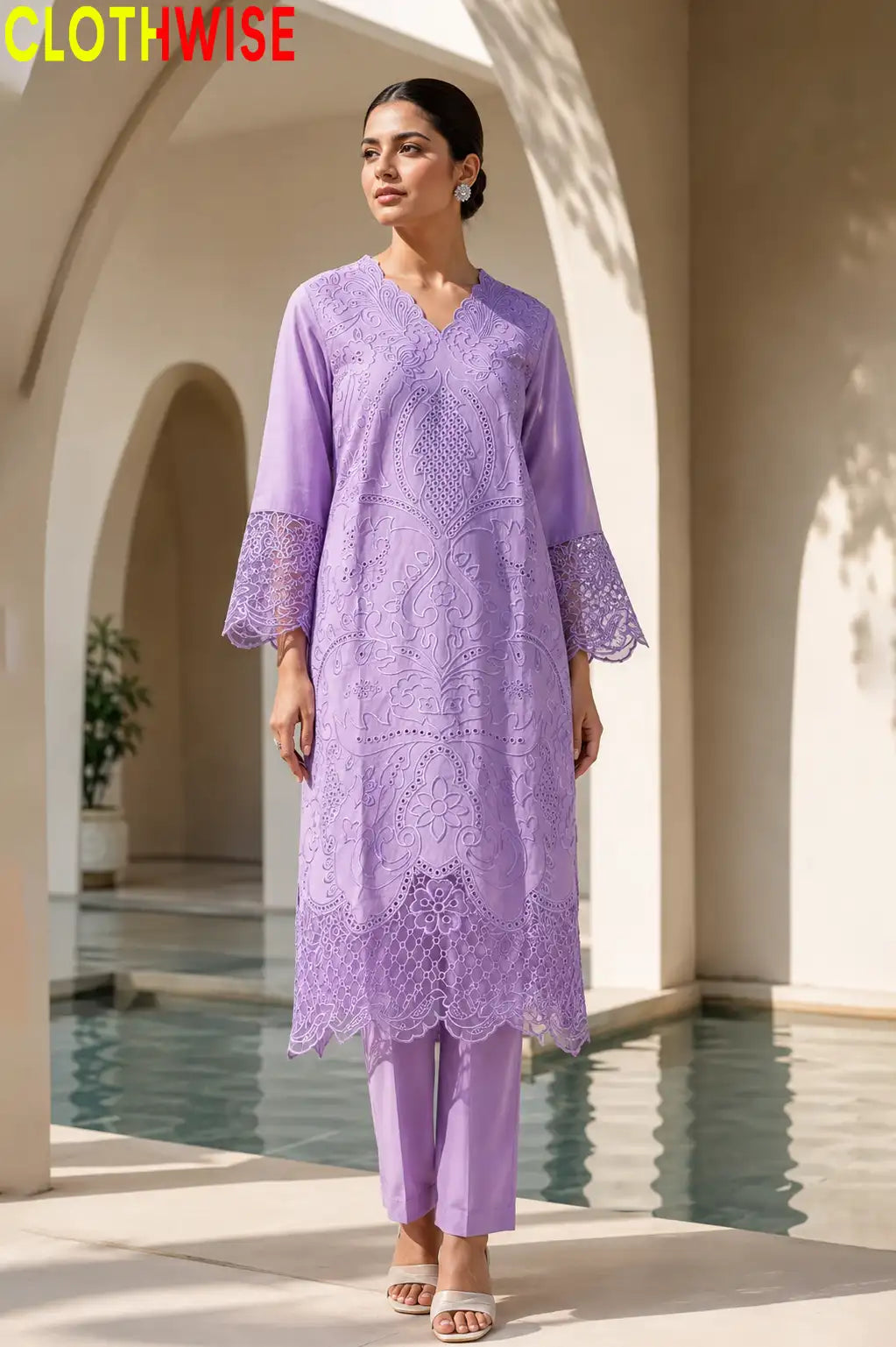 A woman modeling a lavender purple ethnic kurta set with matching trousers, featuring intricate floral lace embroidery, set against an elegant outdoor patio with arches and a pool.