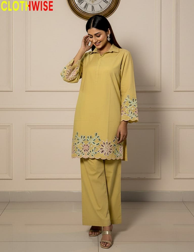 Woman wearing a yellow outfit with floral embroidery in a room with a clock on the wall.