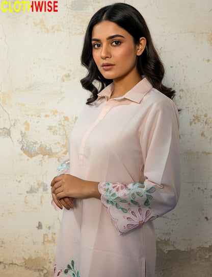 Woman wearing a light pink blouse with floral sleeves against a textured wall.