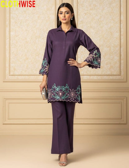 Woman wearing a purple outfit with floral embroidery against a beige wall.