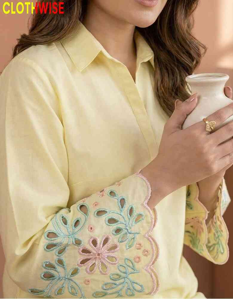 Woman wearing a light yellow shirt with floral embroidery, holding a white ceramic cup.