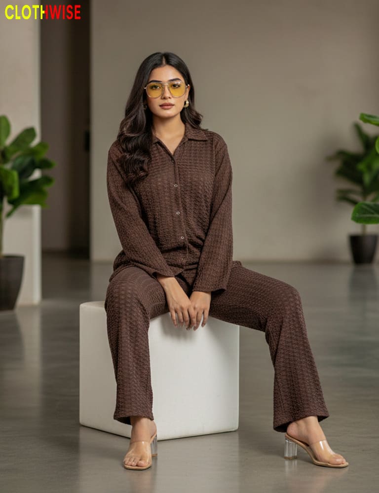 Woman in a brown outfit sitting on a white cube with plants in the background