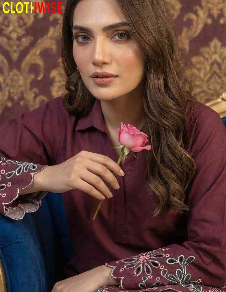 Woman holding a pink rose wearing a maroon embroidered outfit with a patterned background.