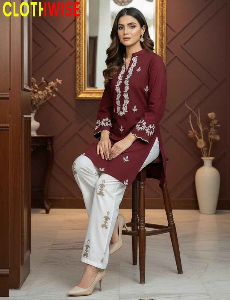 Woman in maroon and white embroidered outfit sitting on a stool in a room with wooden walls and decor.