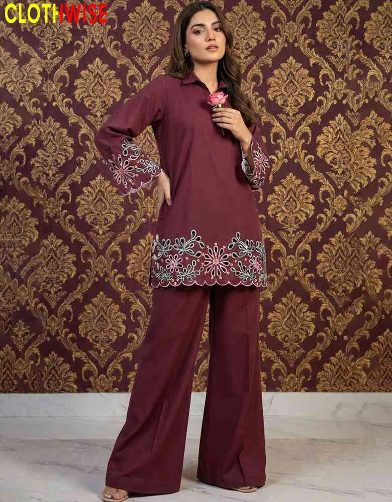 Woman wearing a maroon outfit with embroidery against a patterned wall.