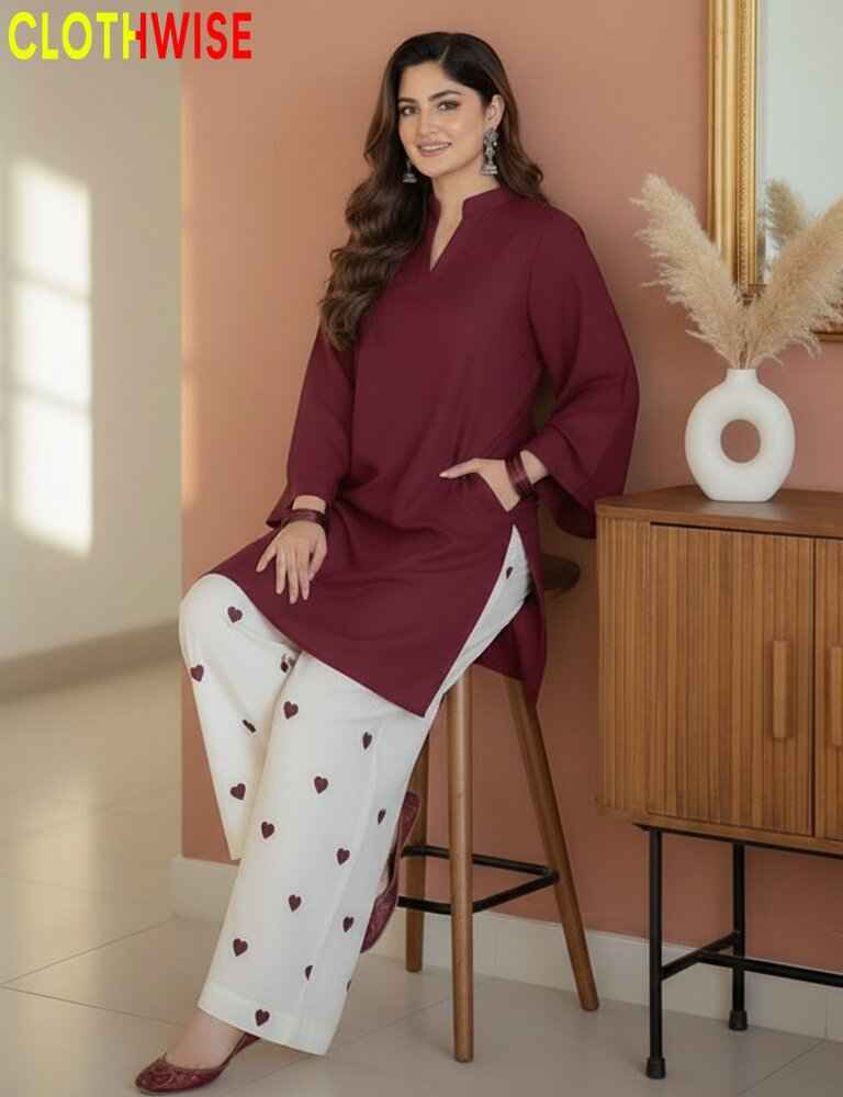 Woman in maroon top and white pants with heart patterns sitting on a stool against a peach wall.