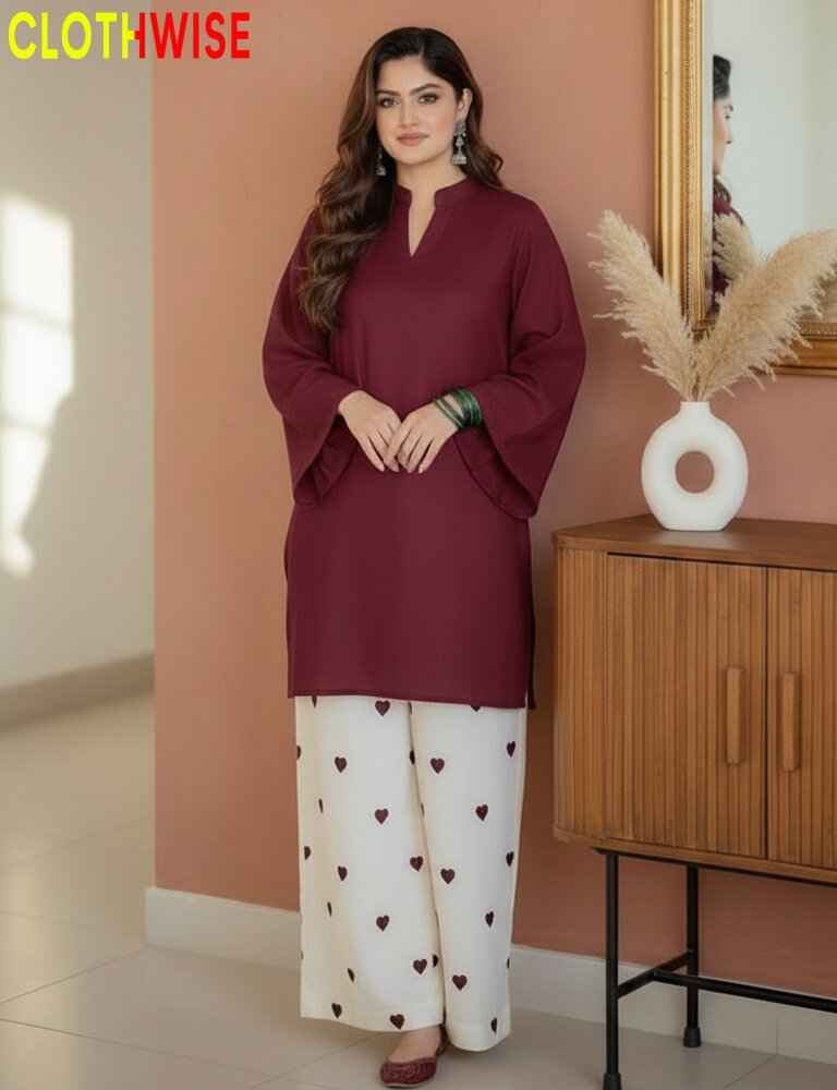Woman wearing a maroon top and white pants with heart patterns, standing in a room with a wooden cabinet and decorative items.