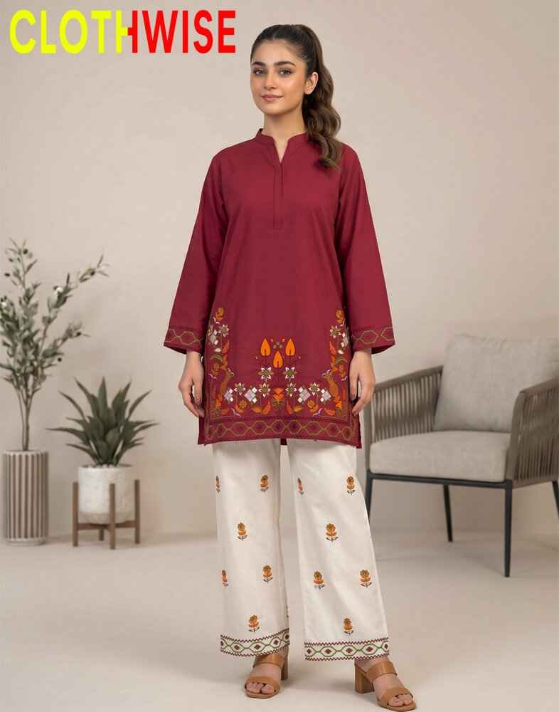 Woman wearing a maroon top and white pants with embroidery, standing in a room with plants and a chair.