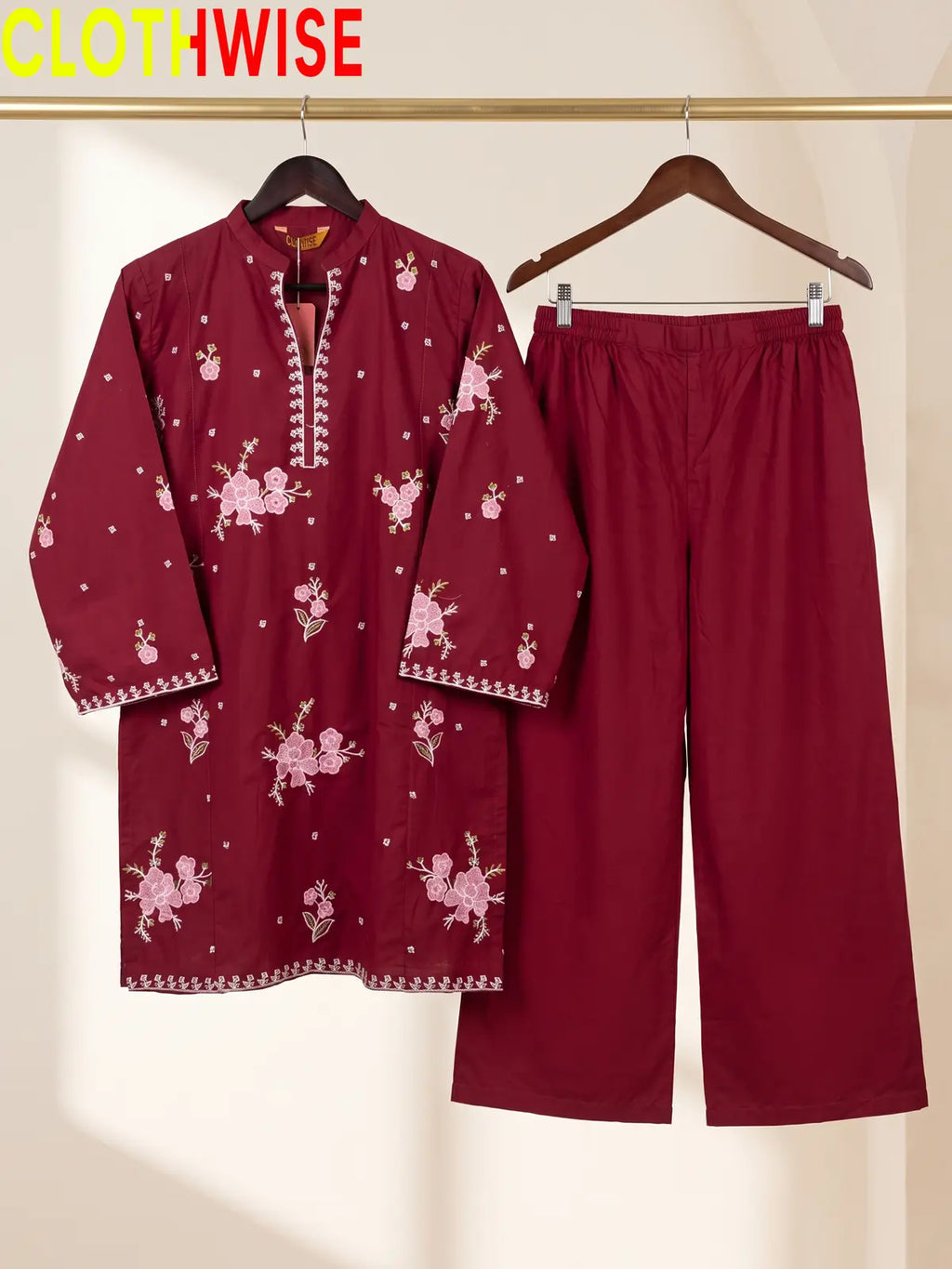 Hanger display of a maroon 2-piece stitched outfit featuring a floral embroidered straight shirt and matching wide-leg trousers on a golden metal rack