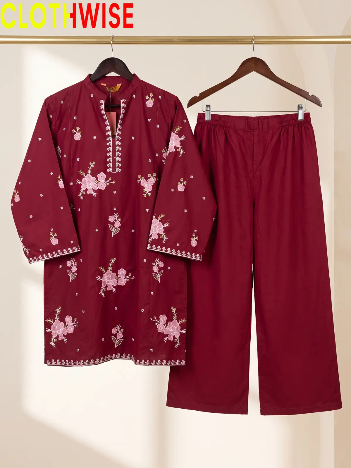 Hanger display of a maroon 2-piece stitched outfit featuring a floral embroidered straight shirt and matching wide-leg trousers on a golden metal rack