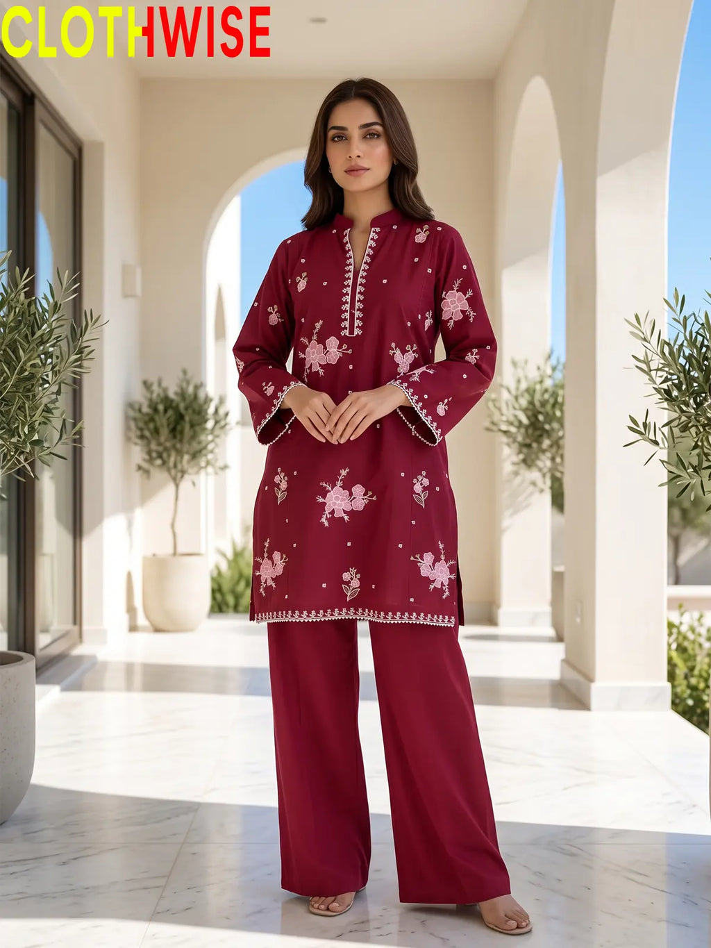 Front view of a model wearing a maroon embroidered straight tunic and matching palazzo pants against an outdoor arches backdrop