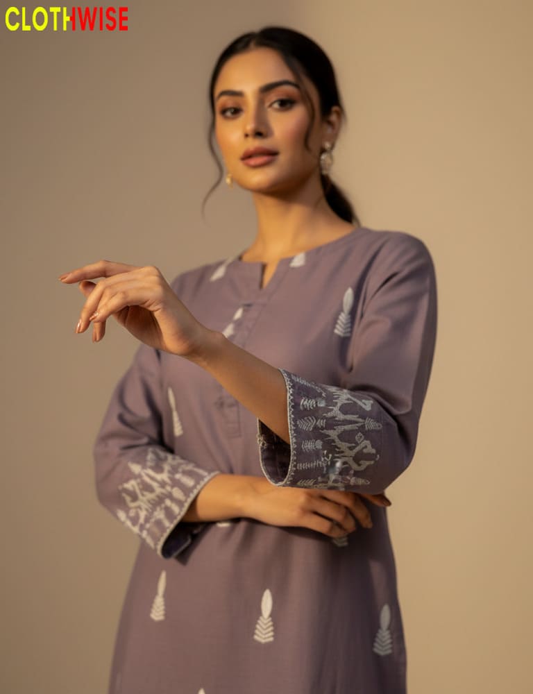 Woman wearing a purple kurta with white patterns, posing against a beige background.