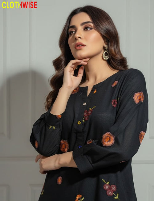 Woman wearing a black outfit with floral embroidery, posing against a neutral background.
