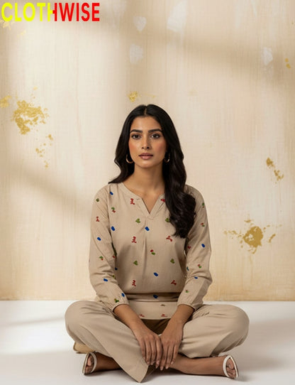 Woman wearing a beige outfit with colorful patterns sitting on a white surface against a beige background with floral designs.