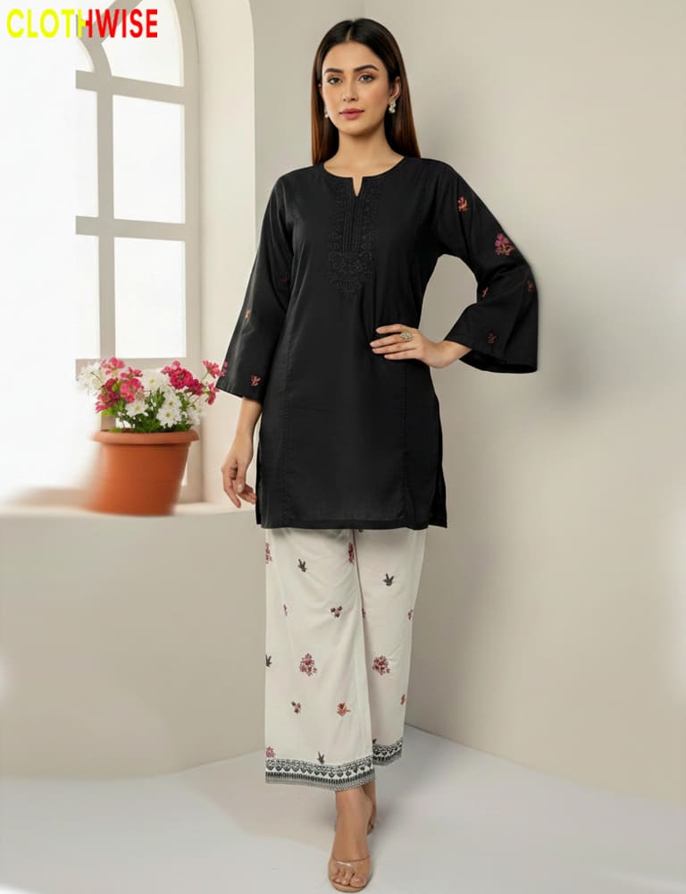 Woman wearing a black top and white pants with floral patterns, standing indoors.