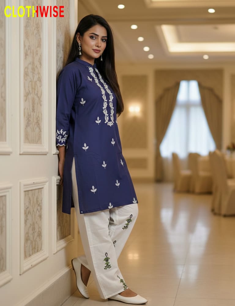Woman wearing a blue embroidered top and white pants in an elegant indoor setting.