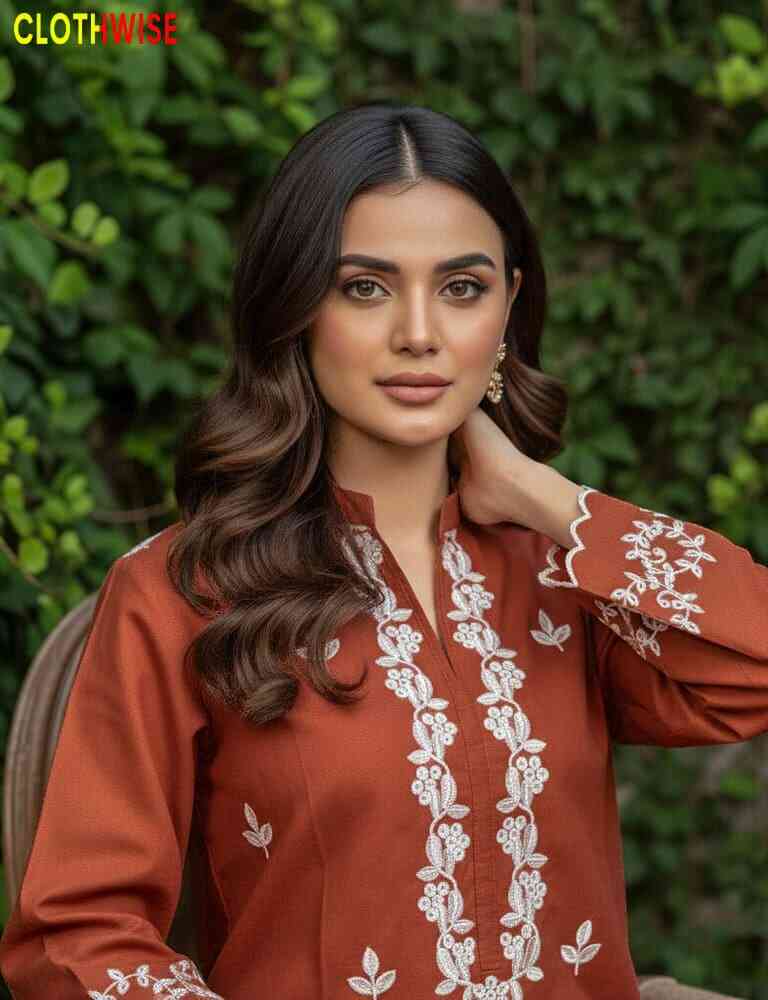 Woman wearing a rust-colored embroidered top with white patterns against a green leafy background.