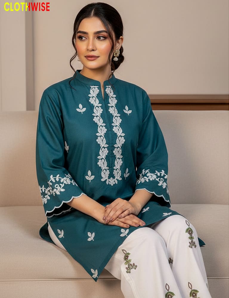 Woman wearing a teal embroidered kurta with white pants sitting on a beige couch.