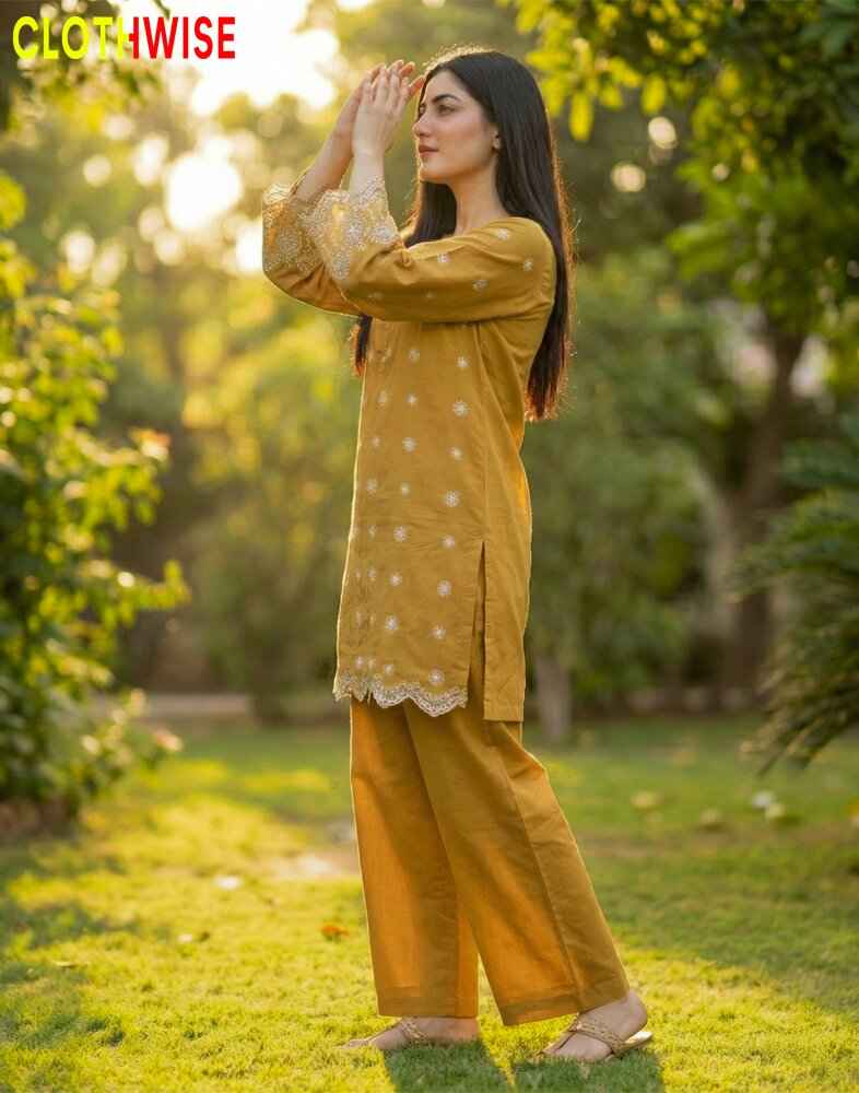 Woman in a mustard yellow outfit standing in a garden with trees and sunlight.