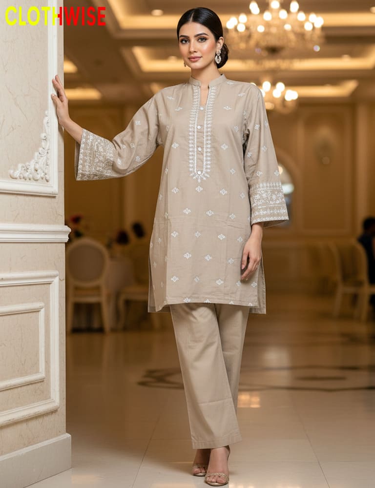 Woman in a beige outfit with white patterns standing in an elegant indoor setting.