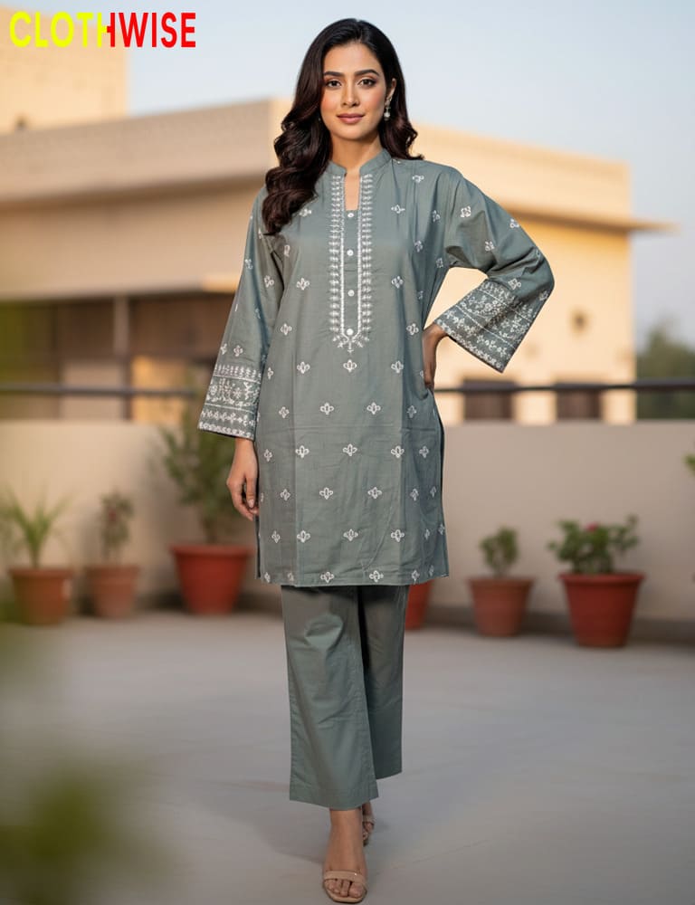 Woman wearing a gray embroidered outfit with a blurred background of plants and a building.