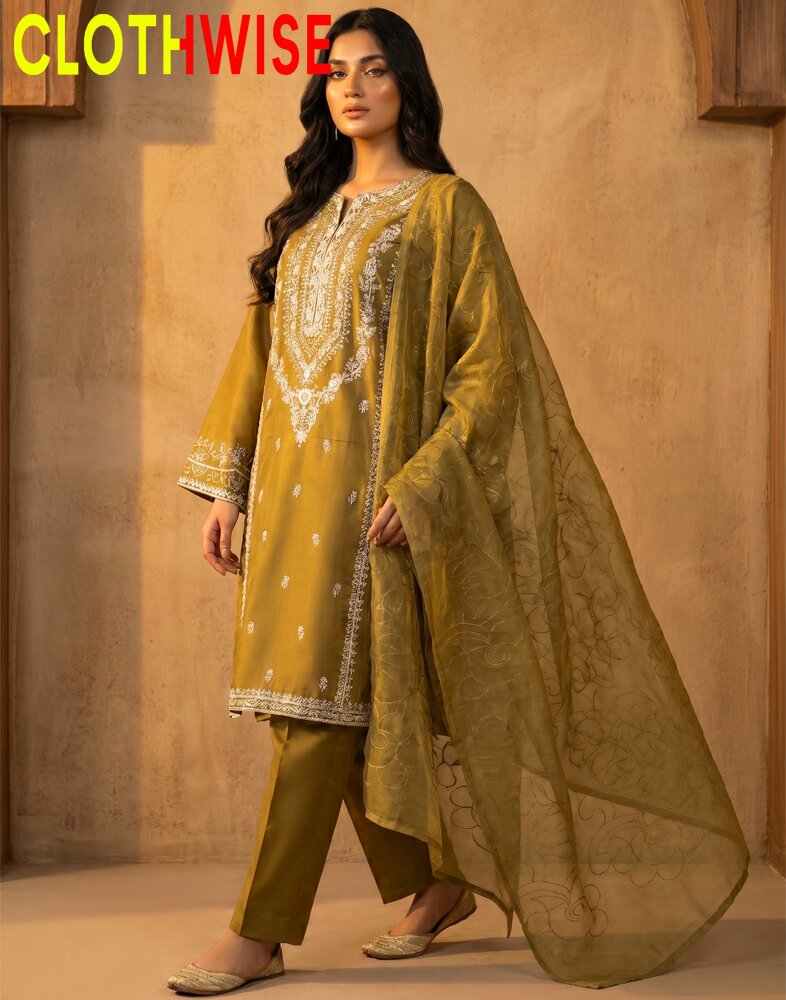 Woman wearing a mustard yellow embroidered outfit with a dupatta, standing against a beige wall.