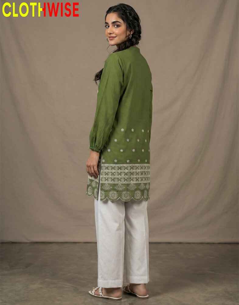 Woman wearing a green embroidered top and white pants with 'CLOTHWISE' branding.