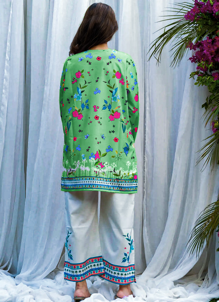 Person wearing a green floral embroidered top with white pants against a white curtain background