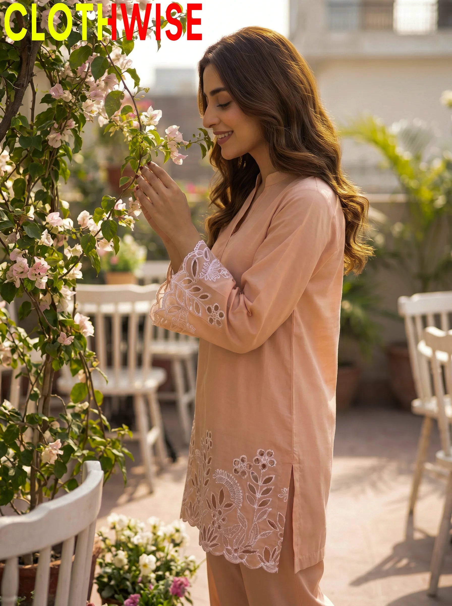 Woman in a peach dress with lace details standing in a garden setting.