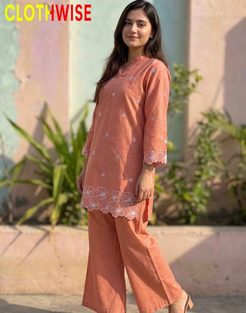 Woman wearing a peach-colored outfit with floral patterns, standing outdoors with plants in the background.