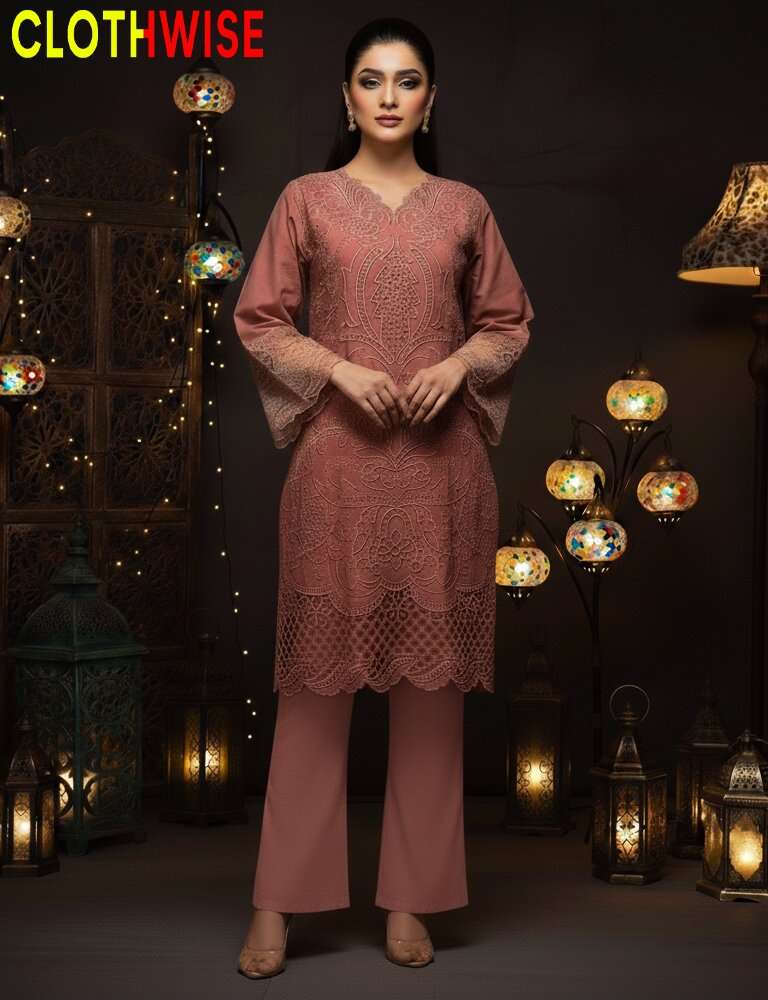 Woman wearing a pink outfit with intricate patterns in a dark setting with decorative lights.