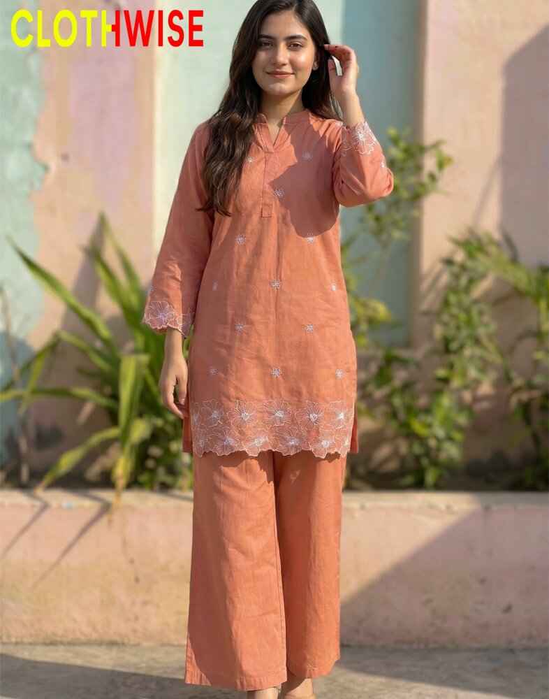 Woman wearing a peach-colored kurta with white embroidery, standing outdoors with plants in the background.