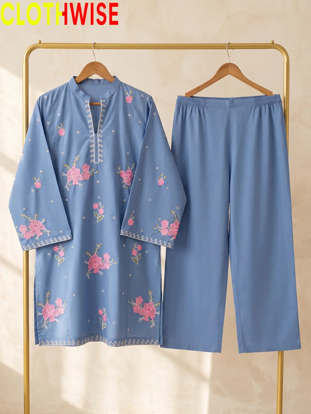Hanger display of a periwinkle blue 2-piece stitched outfit featuring a floral embroidered straight shirt and matching wide-leg trousers on a golden metal rack