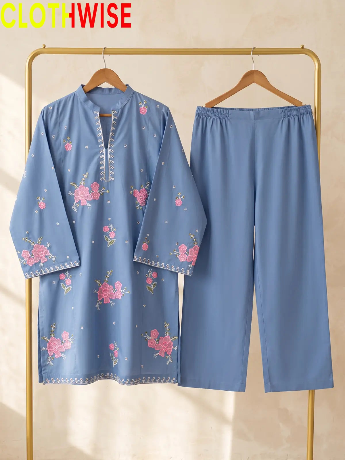 Hanger display of a periwinkle blue 2-piece stitched outfit featuring a floral embroidered straight shirt and matching wide-leg trousers on a golden metal rack